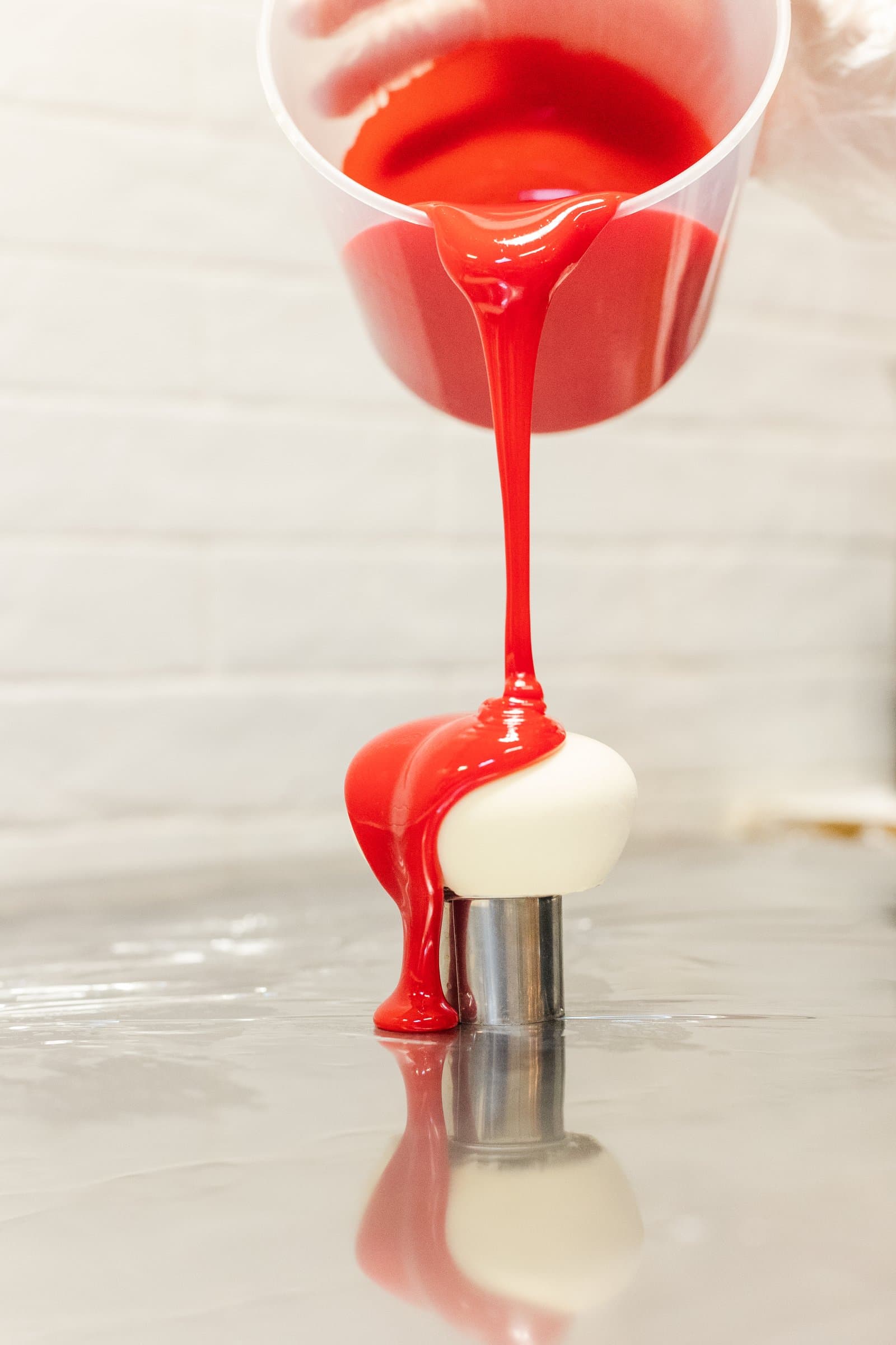 A custom cake being finished with a glossy red glaze