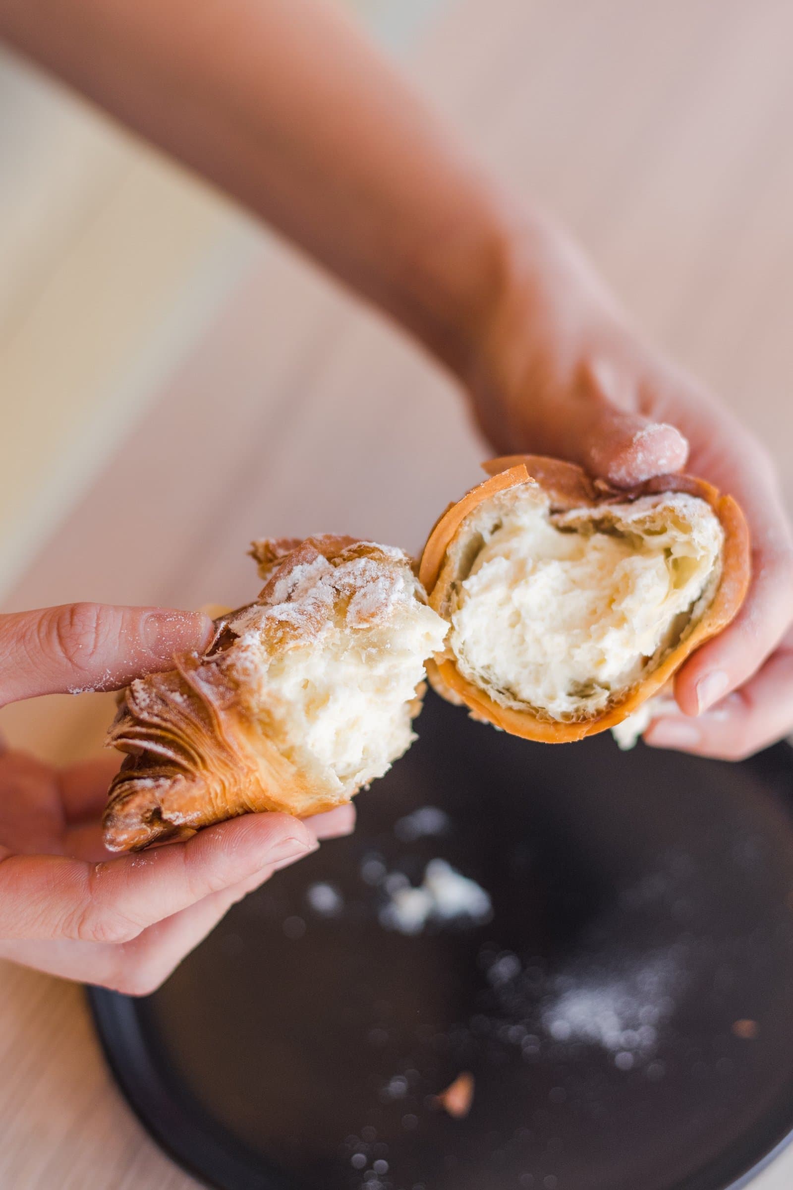 A stuffed croissant torn open by hand, cream filling and powdered sugar visible inside